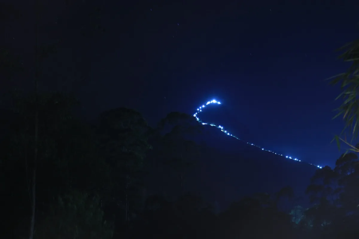 A line of lights tracing the pilgrim path up the dark slope of Adam's Peak to the lit summit at night