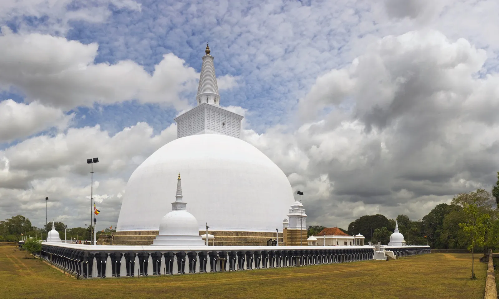 The great white Ruwanwelisaya dagoba in Anuradhapura under a cloudy sky, ringed by a wall of carved elephants