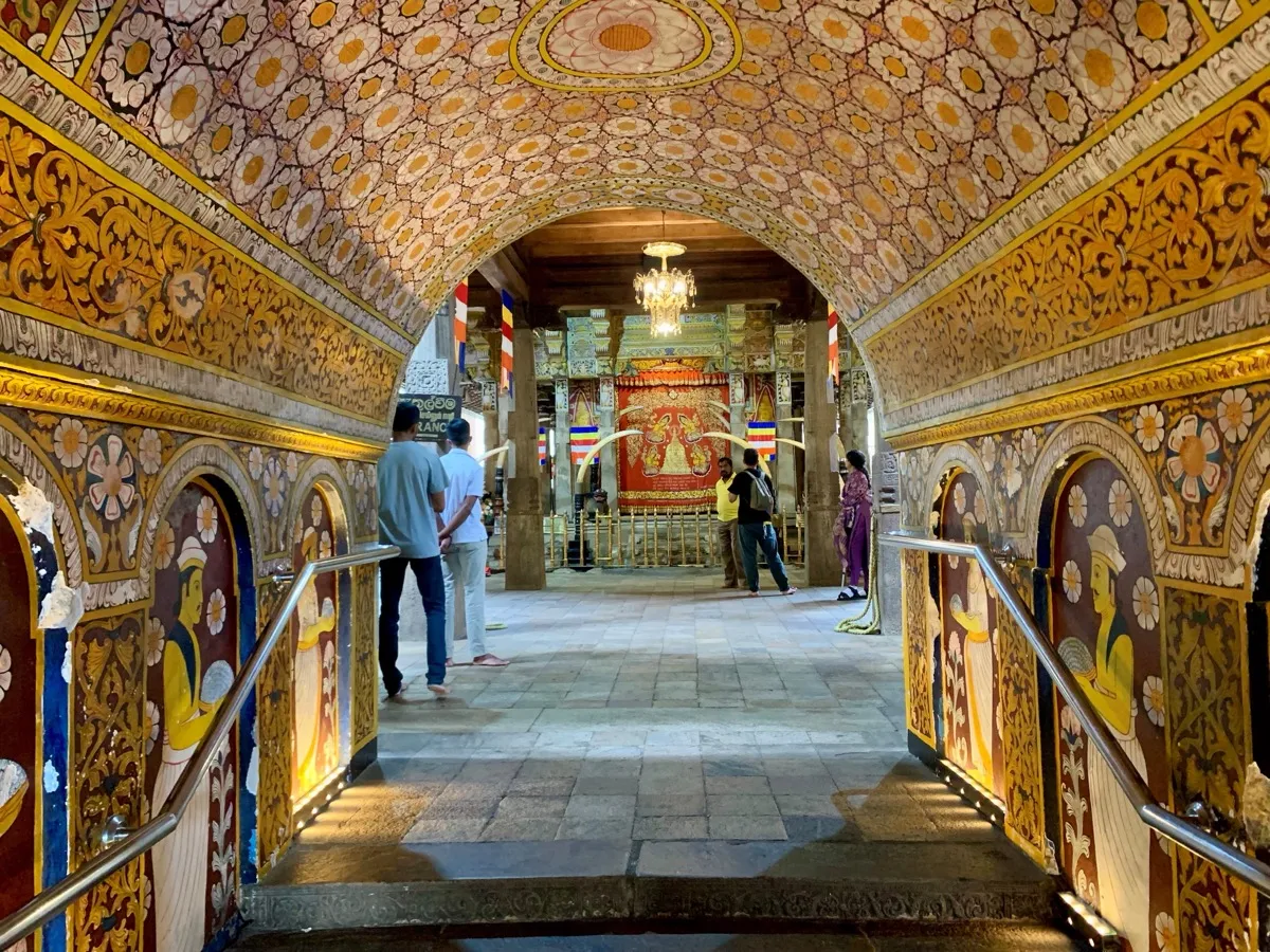The painted, flower-patterned entrance passage of the Temple of the Tooth in Kandy, with barefoot visitors walking through