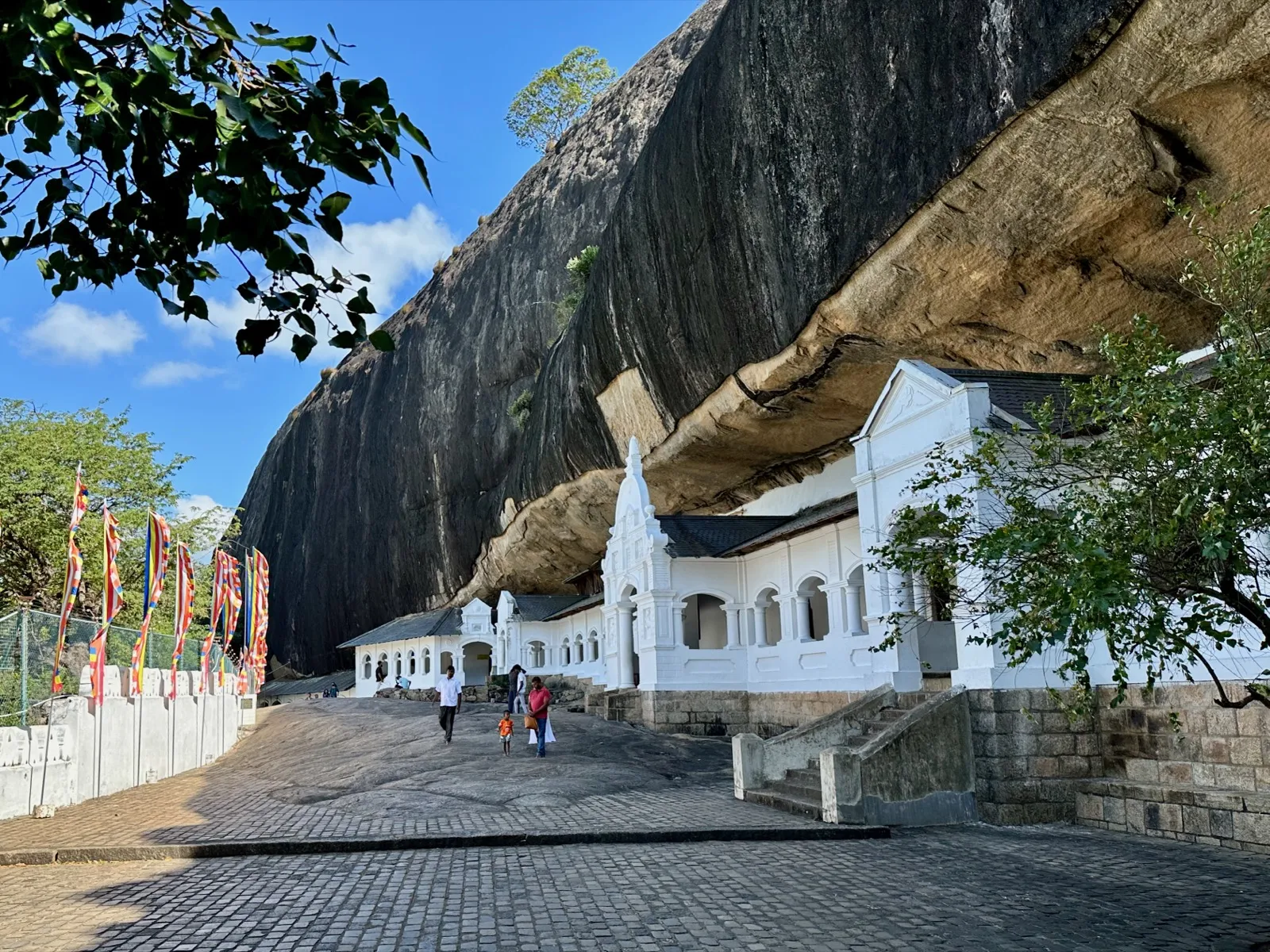 The white arched facade of the Dambulla cave temple sitting beneath a vast overhanging rock