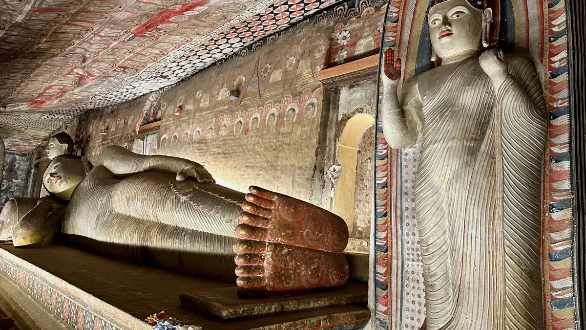 A long reclining Buddha statue and a standing Buddha beneath painted cave ceilings at Dambulla