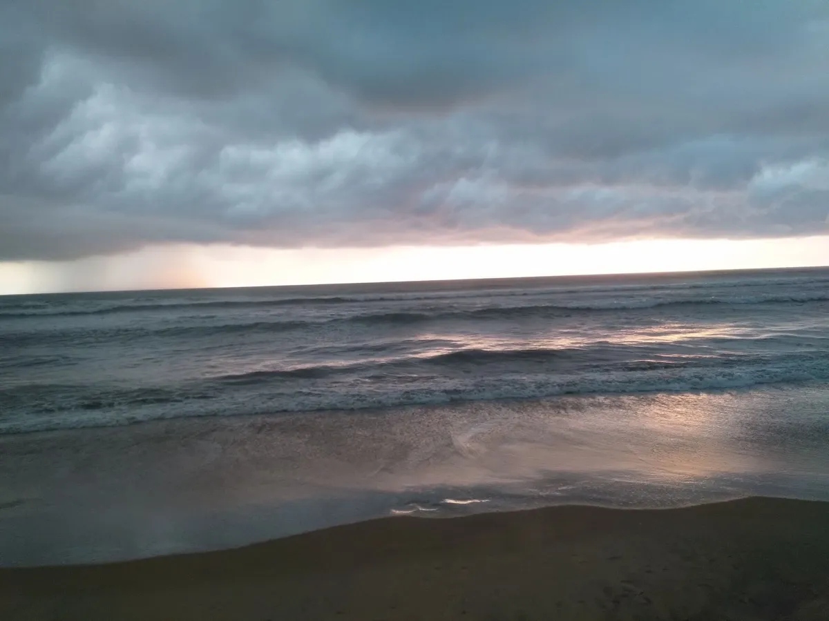 Heavy grey storm clouds rolling in over rough sea and an empty beach, with rain falling on the horizon
