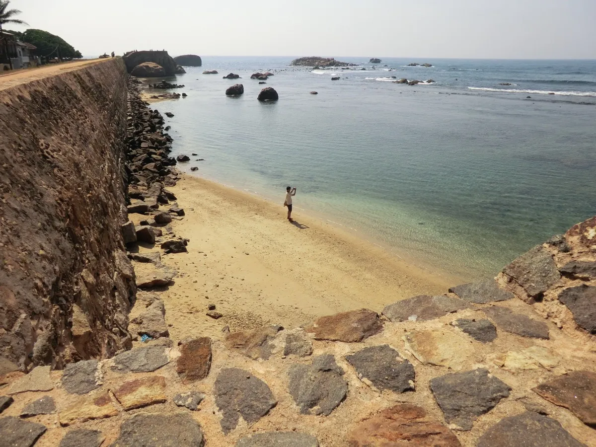 The high stone sea wall of Galle Fort above a small sandy beach, looking along the ramparts towards Flag Rock