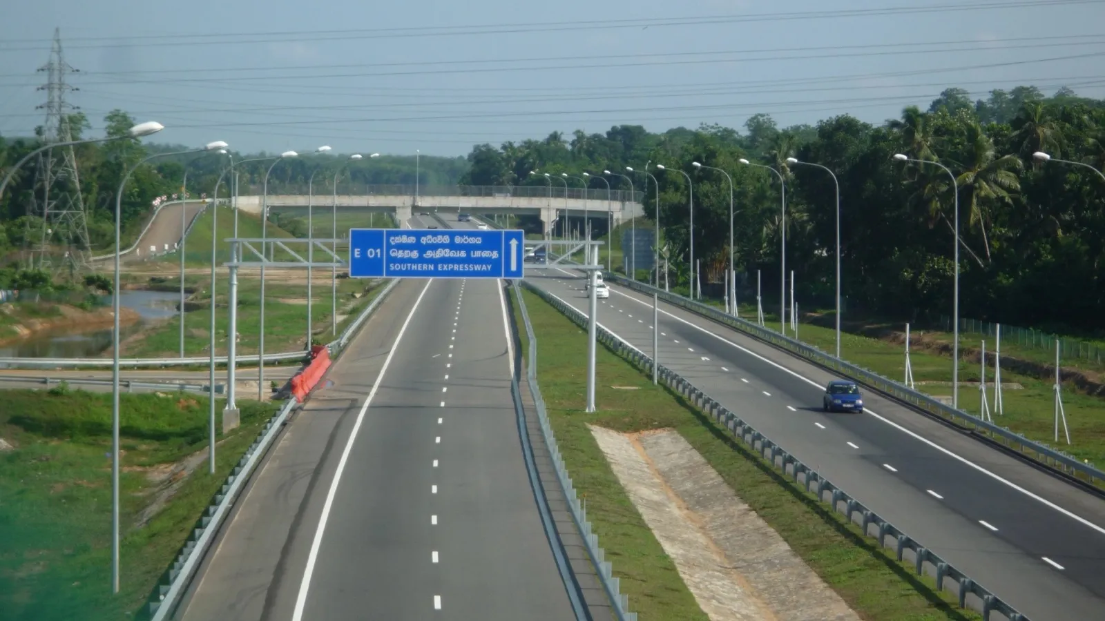 A wide, nearly empty dual carriageway with a blue trilingual 'E01 Southern Expressway' sign, lined with lamp posts and palms