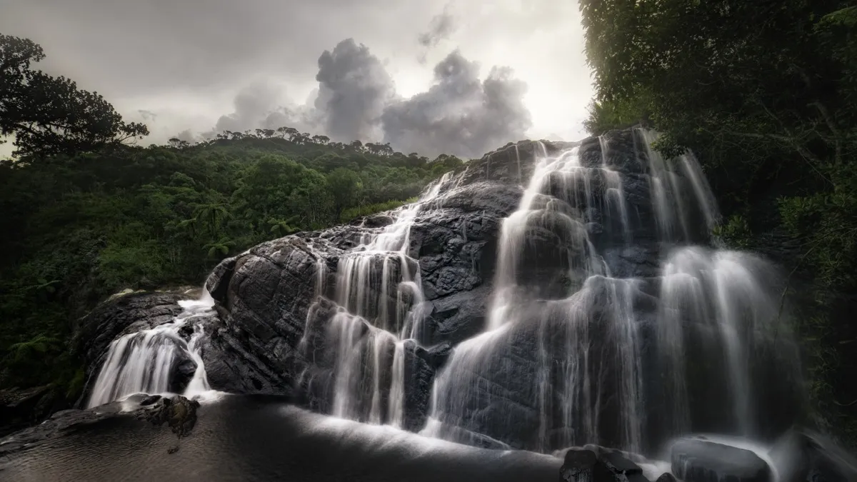 Baker's Falls in Horton Plains, white water spilling in many strands over a broad black rock face under a stormy sky