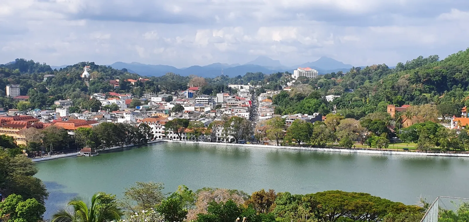 Kandy Lake seen from the hillside viewpoint, with the white buildings of the town, the Temple of the Tooth and green hills stretching to distant mountains