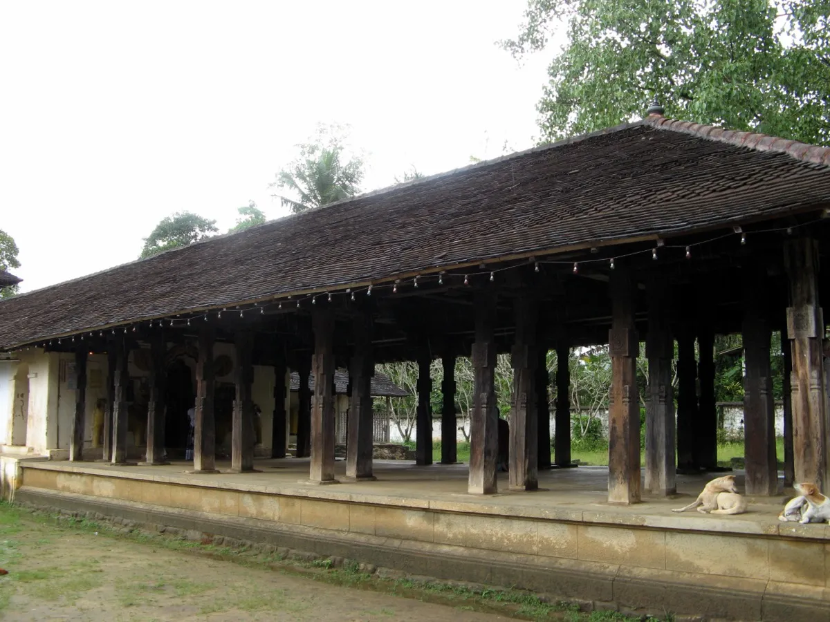 The long open timber hall of Embekke Devalaya with rows of carved wooden pillars under a low tiled roof