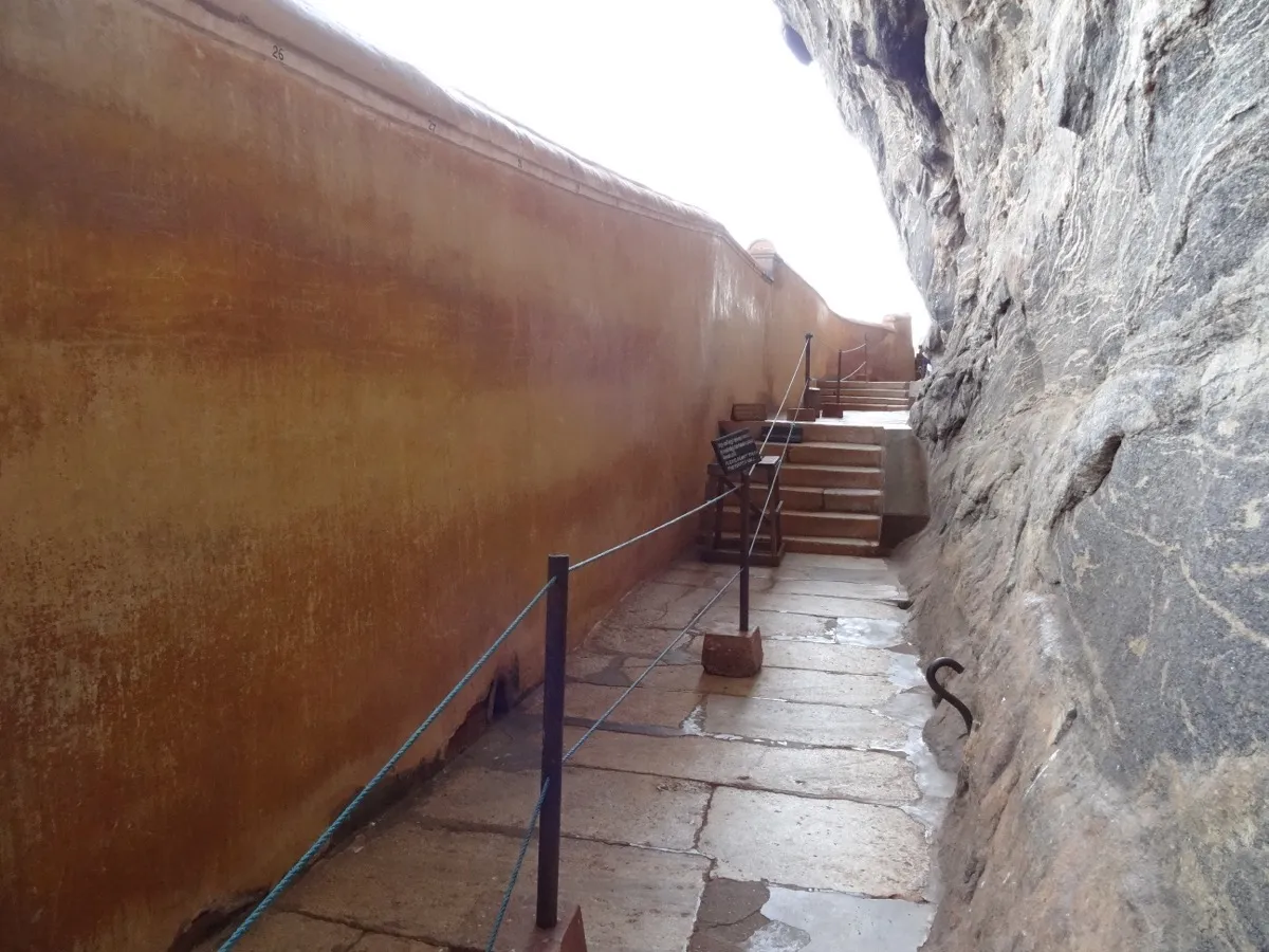 The Mirror Wall at Sigiriya: a long, smooth orange wall beside a narrow stone path under the rock