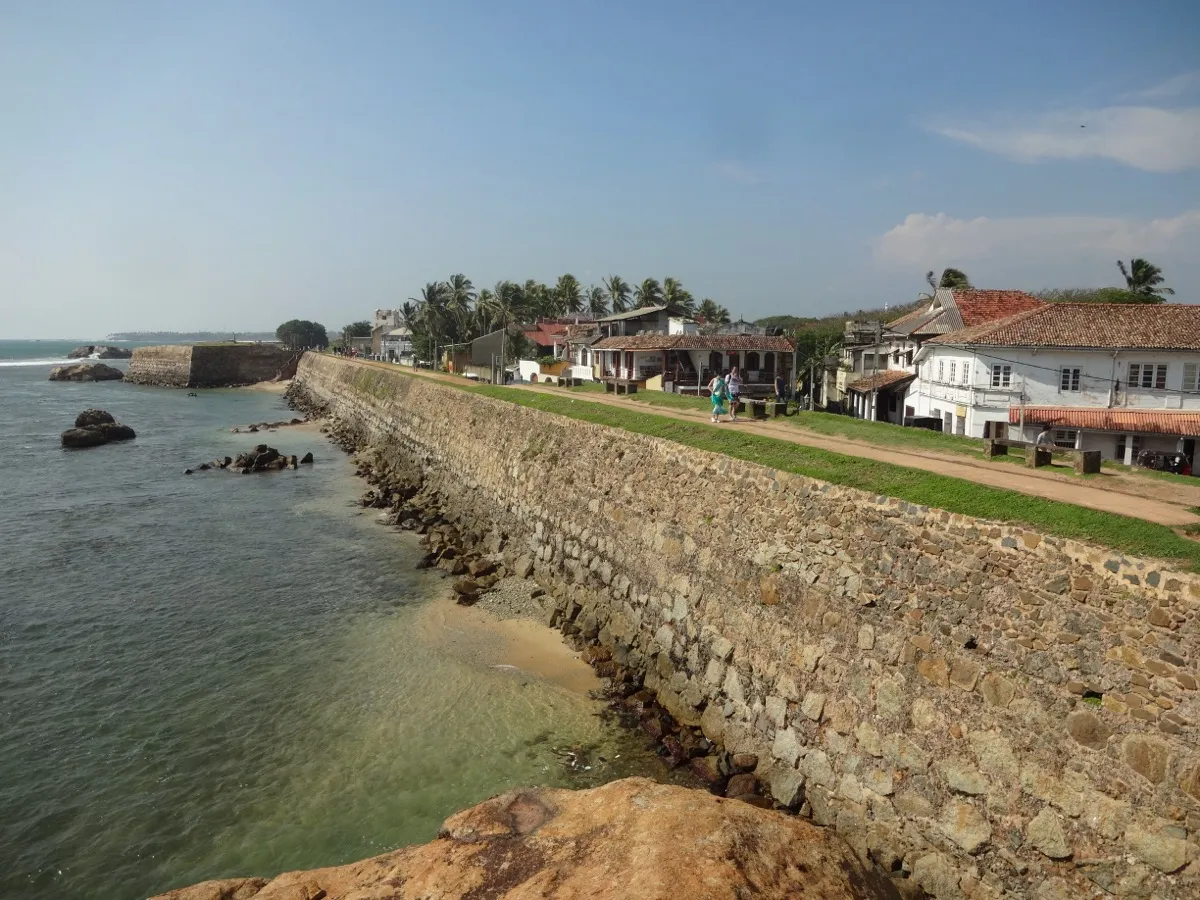 The old stone sea wall of Galle Fort, with a grassy path on top, houses alongside and calm sea below