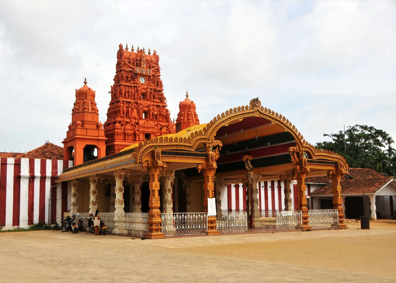 The ornate golden entrance hall and red carved gopuram tower of Nallur Kandaswamy Kovil in Jaffna, framed by red-and-white striped temple walls