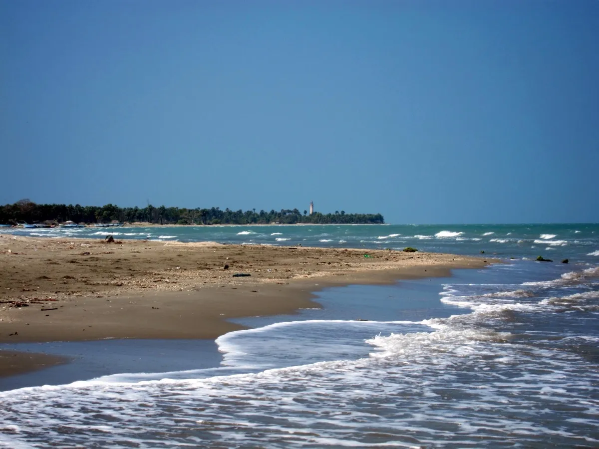 Low waves washing over the flat sand at Casuarina beach near Jaffna, a lighthouse just visible on the distant shore