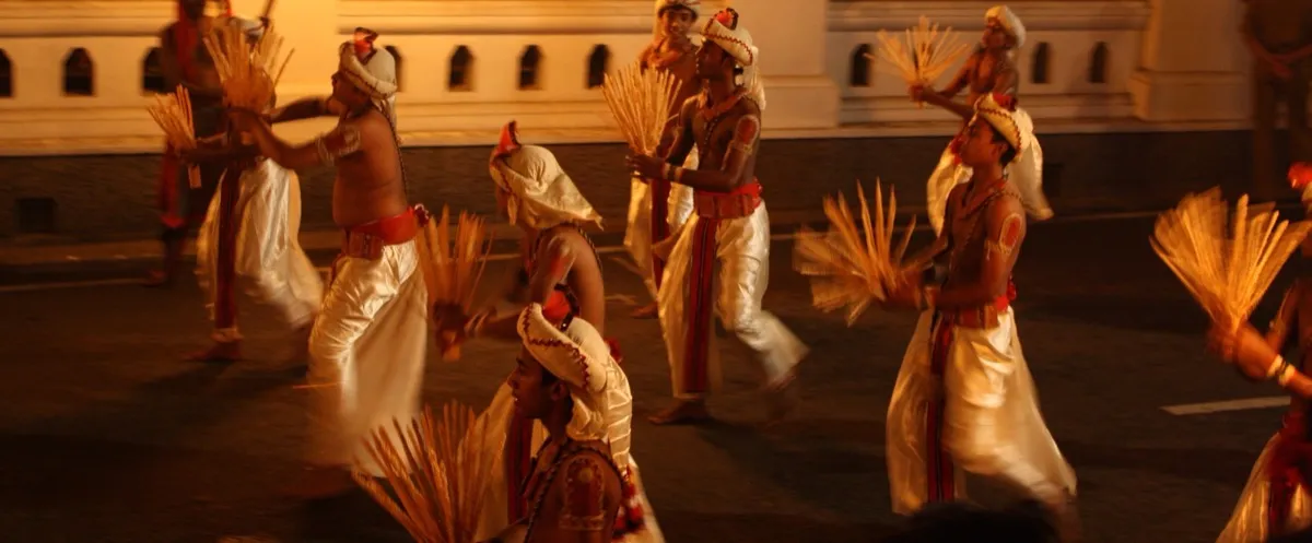 Dancers in white and red costume carrying straw sheaves pass a blazing torch during the Kandy Esala Perahera at night