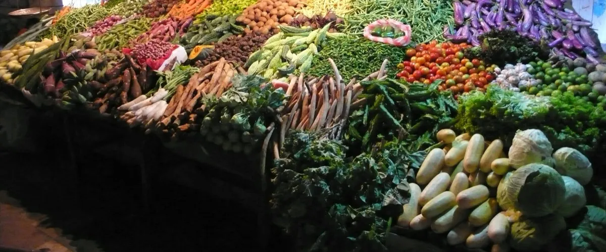 A market stall in Galle heaped with beans, aubergines, tomatoes, carrots and cabbages under a hanging scale