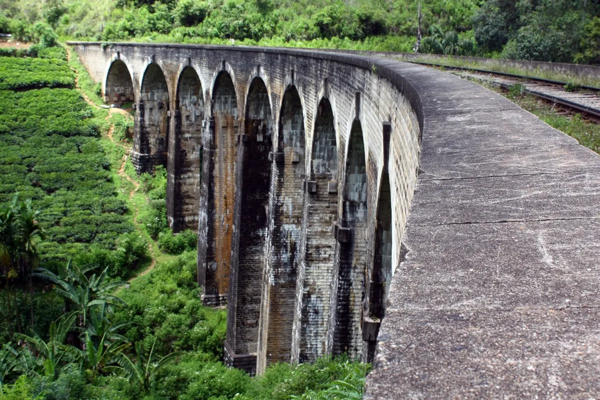 The curving arches of the Nine Arch Bridge near Ella seen from track level, with tea bushes on the slope below
