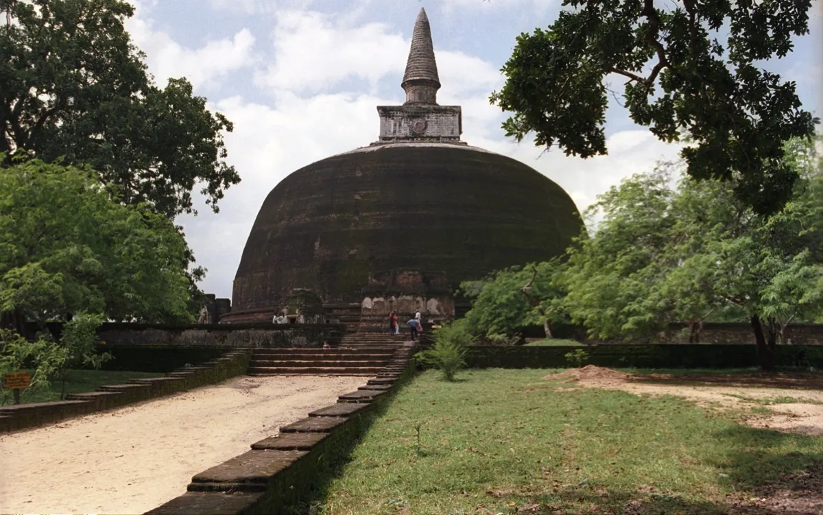 The large dark brick dome of Rankot Vihara in Polonnaruwa with a spire, framed by trees