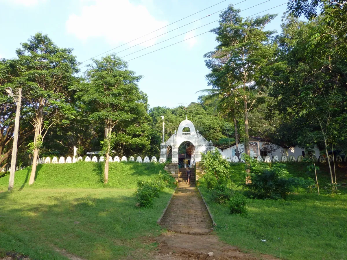 A white arched gateway with steps leading into Pidurangala temple at the foot of the rock