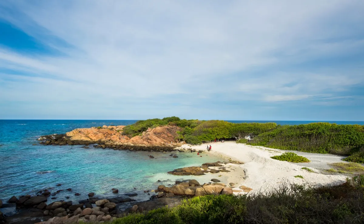 The white coral beach and clear rock-fringed shallows of Pigeon Island National Park off Nilaveli, scrub-covered island behind