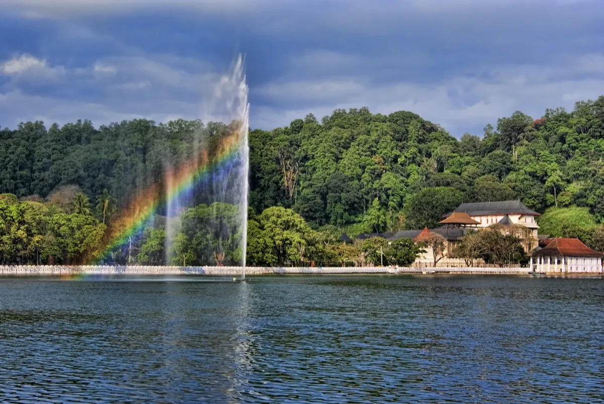 The Temple of the Tooth in Kandy, white buildings with tiled roofs, seen across the lake with a fountain