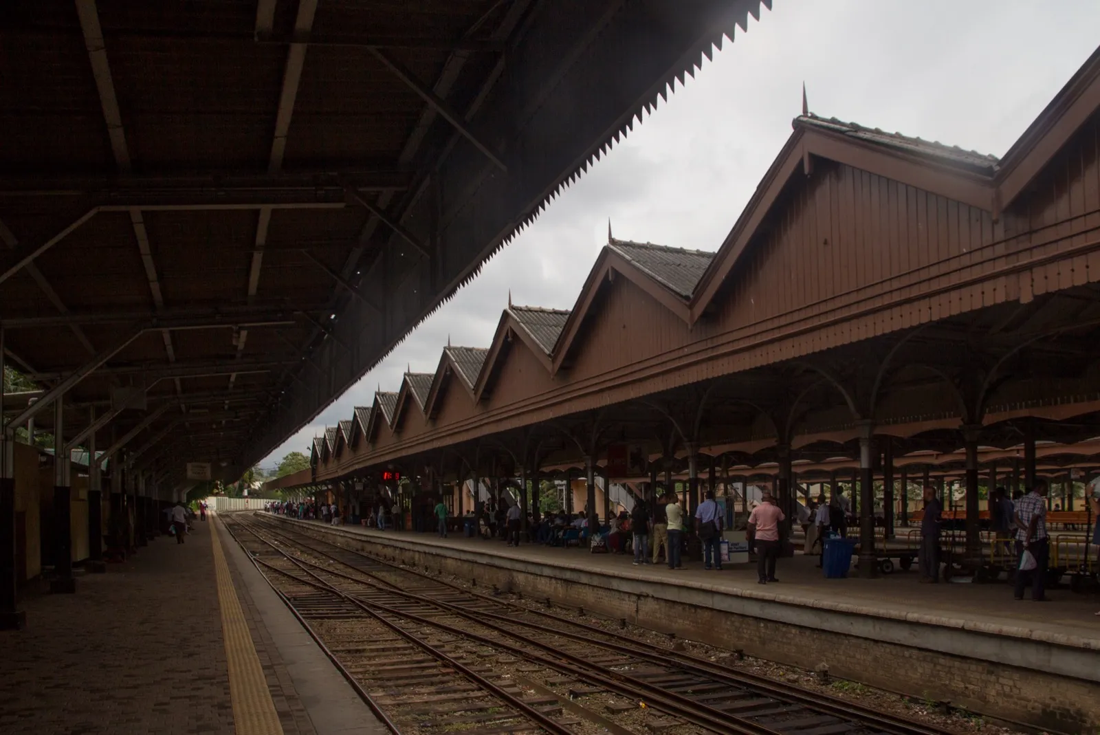 A long covered platform at Colombo Fort railway station, with passengers waiting beside the tracks