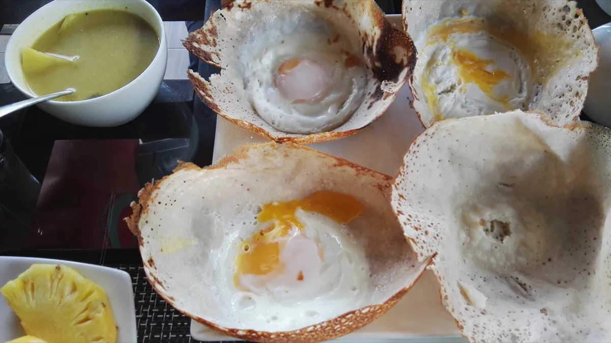 Crisp bowl-shaped egg hoppers with a runny egg in the centre, next to a bowl of curry