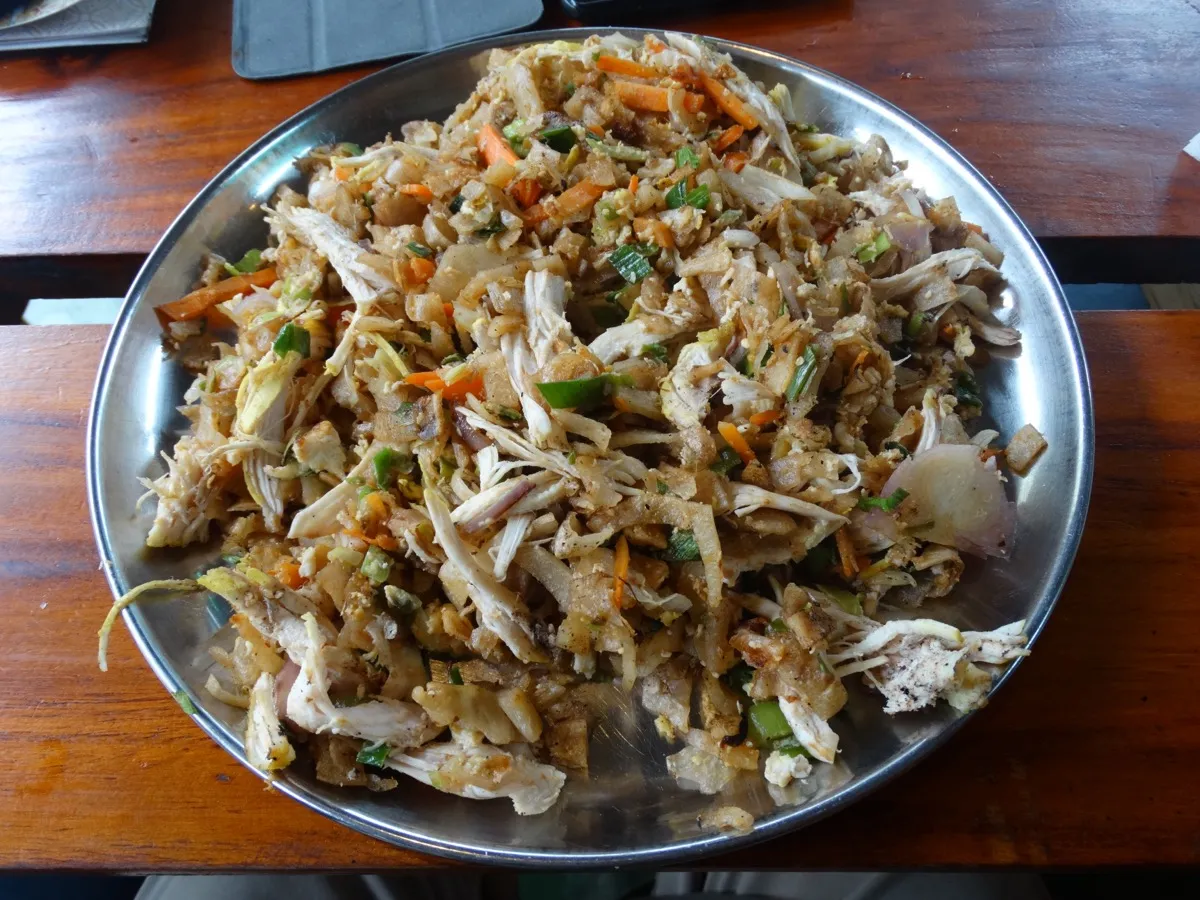 A steel plate piled with chopped chicken kottu roti with carrot, leek and egg