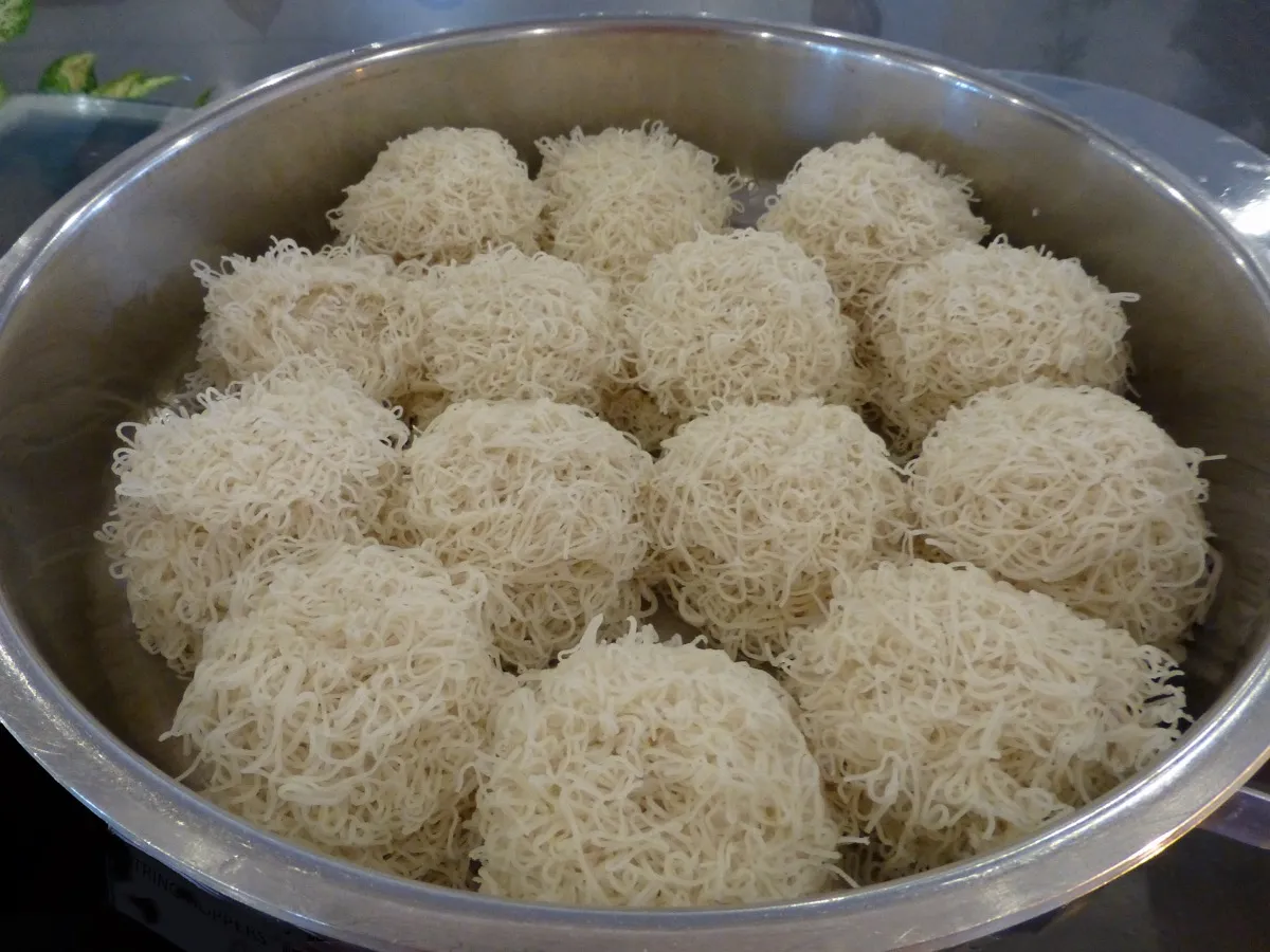 A steamer pan full of small round nests of string hoppers, thin steamed rice-flour noodles