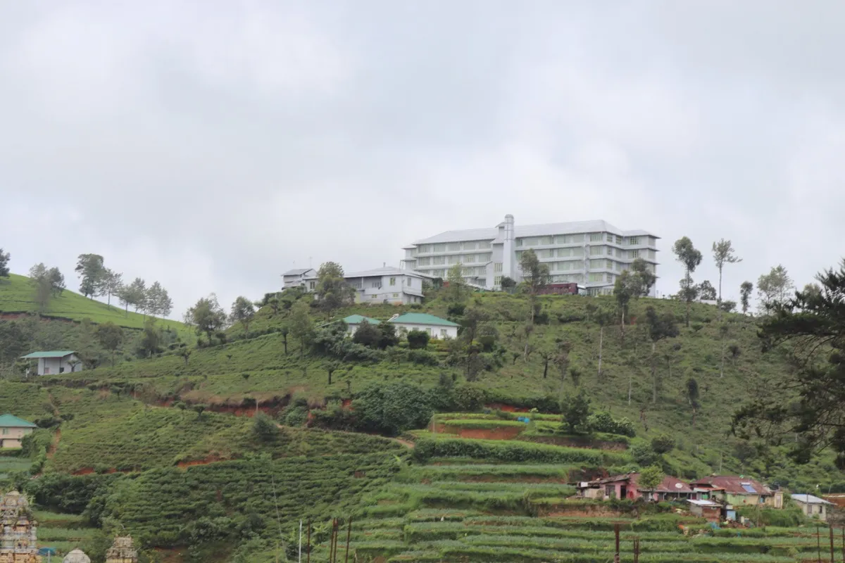 A tall white tea factory on a hilltop above terraced tea bushes and estate houses near Nuwara Eliya