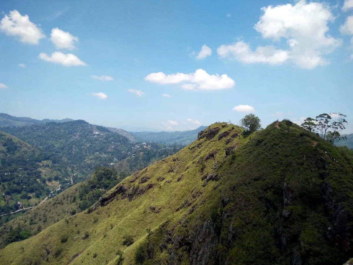 The steep grassy ridge of Little Adam's Peak with its footpath along the crest and Ella town spread across the valley beyond