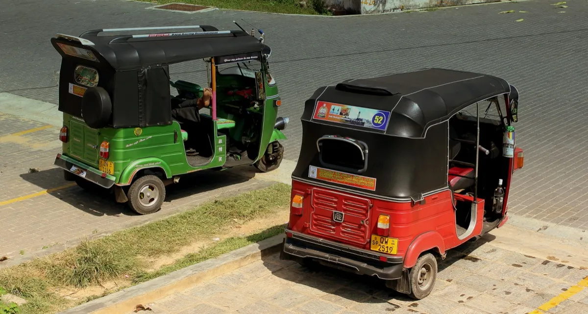 Two tuk-tuks, one green and one red with a black roof, parked on a paved street in Galle Fort