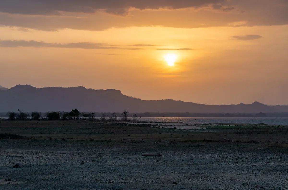 Sunset over the low water of Udawalawe reservoir, with dark hills of the central highlands on the horizon